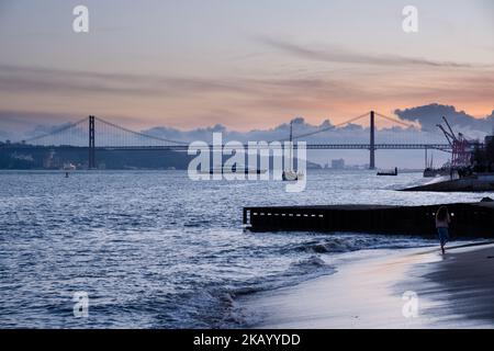 LISSABON-ABEND: Blick auf die Brücke Ponte 25 de Abril und Santuário de Cristo Rei auf der Promenade Tejo entlang des Flusses Tejo (Rio Tejo) Strand und Wellen Stockfoto