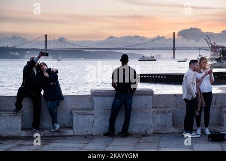 IDYLLISCHER ABEND: Touristen genießen den Blick auf die Brücke Ponte 25 de Abril und Santuário de Cristo Rei an der Promenade Tejo, Fluss Tejo (Rio Tejo), Lissabon Stockfoto