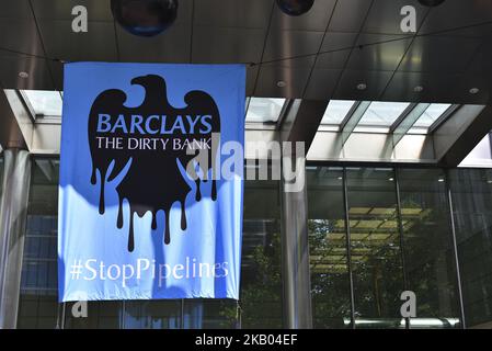 Greenpeace-Aktivisten versammeln sich am Haupteingang der Barclays-Bankhedquarters in Canary Wharf, um gegen die Weigerung der Bank zu protestieren, Pipelines zu finanzieren, die Öl aus Kanadas Teersand am 19. Juli 2018 in den USA und Asien, London, auf den Markt bringen. Aktivisten stiegen den Eingang an, um das Headquaters-Zeichen in einem Öltropfeffekt zu beschicken, und andere, die als Banker verkleidet das Gebäude betraten, während sie aufgezeichnete Nachrichten von Barclays-Kunden spielten, die gegen die Finanzierung der Ölsand-Pipelines durch die Bank sind. (Foto von Alberto Pezzali/NurPhoto) Stockfoto