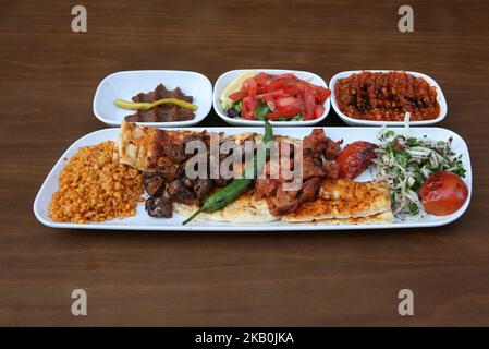 Auf dem Teller stehen Leberkebab und Lammschisch-Kebab, begleitet von Salat, würziger Paste und rohen Fleischbällchen Stockfoto