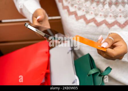 Afroamerikanische Frau sitzt, hält Handy, mit Kreditkarte bezahlen. Stockfoto