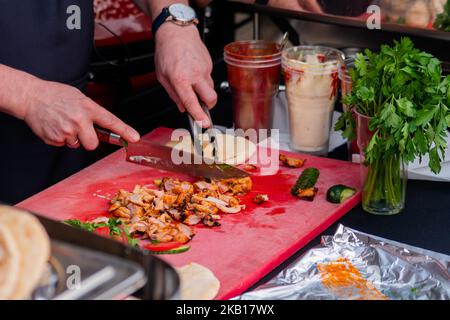 Koch schneidet Hühnerfleisch auf dem Tisch beim Street Food Festival Stockfoto