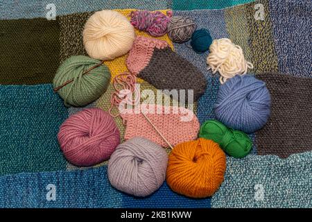 Variety of balls of wool for crochet and knitting on a warm, knitted background with woolen slippers in the making in the middle Stockfoto