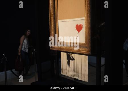 Die Besucher werden am 14. Oktober 2018 im Auktionshaus von Sotheby in London mit dem Titel „Love is in the bin“ der britischen Künstlerin Banksy bebildert. Während des Sotheby's Contemporary Art Sale am 5.. Oktober wurde das Banksy-Kunstwerk „Girl with Balloon“ durch den Boden des Rahmens geschreddert, während es verkauft wurde. Da Banksy für die Aktenvernichtung verantwortlich ist, hat der Käufer zugestimmt, mit dem Verkauf fortzufahren und es trägt nun den Titel 'Love is in the bin' und soll mehr wert sein als die 1,04million Â£, die bezahlt wurden. (Foto von Alberto Pezzali/NurPhoto) Stockfoto