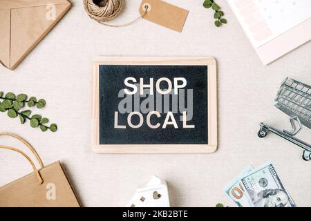 Shop lokaler Text auf Tafel geschrieben. Flat Lay mit Support Local Business Quote, Dekoration und Einkaufstasche, Geschenkboxen und Personal Stockfoto