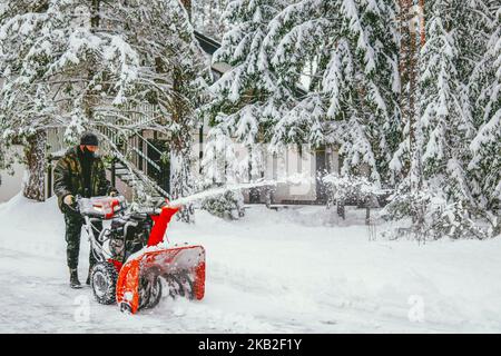 Ein Mann entfernt Schnee mit einem Schneefräsen auf dem Hintergrund eines verschneiten Waldes Stockfoto