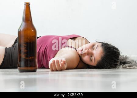 Betrunkene Frau, die auf dem Boden liegt und neben ihr mit einer Flasche Bier schläft. Mädchen mit einer Überdosis Alkohol, die auf dem Boden liegt. Stockfoto