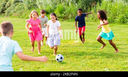 Glückliche Mädchen und Jungen, die auf grünem Rasen Fußball spielen Stockfoto