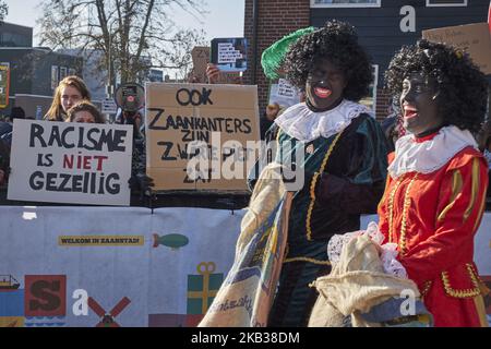 Mehrere als Zwarte Piet verkleidete Personen passieren vor der Demonstration der antirassistischen Gruppe in Zaandam, Niederlande, am 17. November 2018. Der heilige Nikolaus kommt noch ein Jahr von Spanien nach Holland. Dieses Jahr wurde dieses Fest in der Stadt Zaandam, die für ihre malerischen Windmühlen berühmt ist, landesweit gefeiert. Von dort aus wird der Nikolaus in die übrigen niederländischen Städte fahren. Wieder einmal wurde die Feier von der Kontroverse beeinflusst, die von antirassistischen Gruppen geschaffen wurde, die diese Tradition des Habens rassistischer Komponenten beschuldigen. Insbesondere in der Figur von Zwarte Piet, ein ch Stockfoto