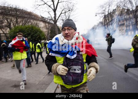 Ein „Gilets Jaunes“ („Gelbe Weste“)-Protestler, der am 15. Dezember 2018 aus Tränengaskanistern um die Champs Elysees Avenue in Paris gelaufen ist. Obwohl die französischen Minister an die landesweiten Proteste der „Gilets Jaunes“ („Gelbwesten“) appellieren, nach dem Anschlag in Straßburg, bei dem am 11. Dezember drei Menschen getötet wurden, aufzuhören, gingen die Demonstranten am fünften Samstag in Folge auf die Straßen Frankreichs. Die Bewegung „Gilets Jaunes“ („Gelbe Weste“), die am 17. November 2018 begann und von der Opposition gegen eine neue Kraftstoffsteuer inspiriert wurde, hat eine breite Palette von regierungsfeindlichen Stimmungen absorbiert und Paris und so zerstört Stockfoto