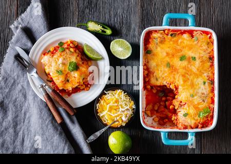 Vegetarische Enchilada-Kasserolle mit Tortillas, Sauce, Pinto-Bohnen, Mais, Zucchini und mexikanischem Käse in Backform und auf Teller, flach Stockfoto