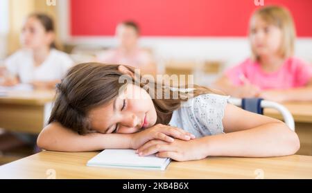 Müde Schulmädchen schlafen am Schreibtisch im Klassenzimmer Stockfoto