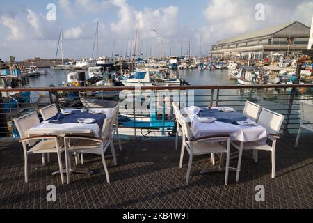 TEL AVIV, ISRAEL - 2. MÄRZ 2017 : Tische und Stühle in einem Restaurant in der Jaffa Hafenpromenade, vor Schiffen, die am Hafen ankern, Tel aviv, I Stockfoto