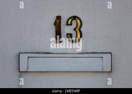 Nahaufnahme eines weißen Briefkastens und der Nummer 13 (dreizehn) an der rauen Außenwand des Hauses. Konzept von schlechten Nachrichten, Aberglauben oder Glück Stockfoto