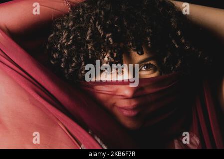 Porträt einer schönen Frau mit einem dünnen Tuch von dunkelroter Farbe auf ihrem Gesicht vor schwarzem Hintergrund. Reife Frau. Selbstwertgefühl-Konzept. Stockfoto