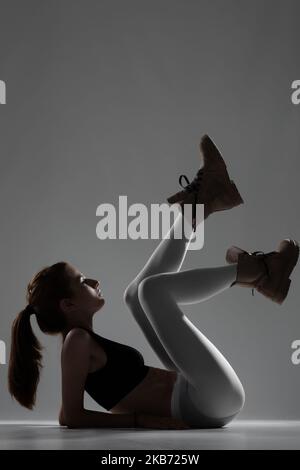 Fit Mädchen mit weißen Leggings und wasserdichte Stiefel. Seitlich beleuchtete Halbsilhouette. Stockfoto