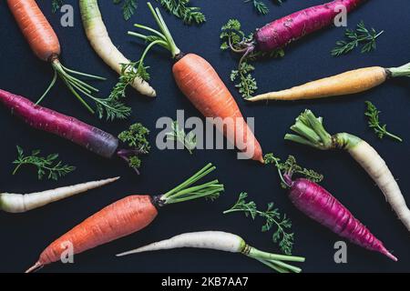 Buntes Karottenmuster auf schwarzem Hintergrund, Regenbogenkarotten flach liegend, Draufsicht Stockfoto