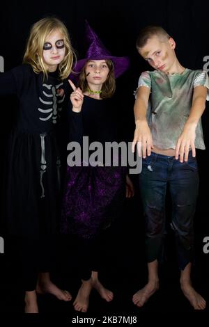 Drei Kinder verkleiden sich für halloween vor einem schwarzen Hintergrund Stockfoto