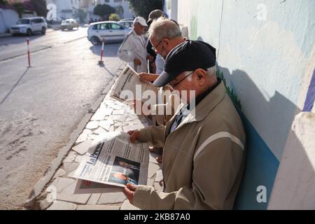 Ein Mann liest eine Zeitung mit einem Titelbild, auf dem die Präsidentschaftskandidaten Kais Saied und Nabil Karoui am 13. Oktober in der Stadt Ennasr, im Gouvernement Ariana, nordöstlich von Tunesien, vor einem Wahllokal Schlange stehen, um seine Stimme für die Stichwahl abzugeben. 2019. (Foto von Chedly Ben Ibrahim/NurPhoto) Stockfoto