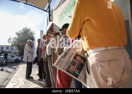Ein Mann hält eine Zeitung mit einem Titelbild, das die Präsidentschaftskandidaten Kais Saied und Nabil Karoui zeigt, als er sich am 13. Oktober in der Stadt Ennasr, im Gouvernement Ariana, nordöstlich von Tunesien, vor einem Wahllokal anstellt, um seine Stimme für die Stichwahl abzugeben. 2019. (Foto von Chedly Ben Ibrahim/NurPhoto) Stockfoto