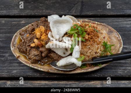 Rending Daging, scharfes indonesisches Eintopf-Rindfleisch und Nasi Goreng, indonesischer oder balinesischer scharfer gebratener Reis auf einem rohen Holztisch. Stockfoto