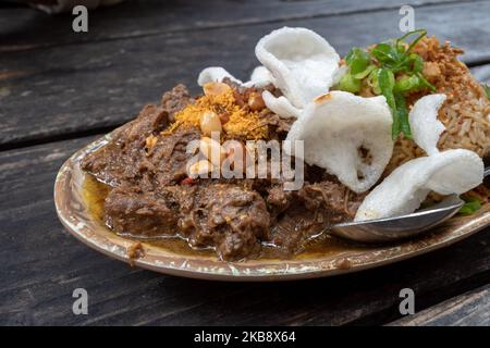 Rending Daging, scharfes indonesisches Eintopf-Rindfleisch und Nasi Goreng, indonesischer oder balinesischer scharfer gebratener Reis auf einem rohen Holztisch. Stockfoto