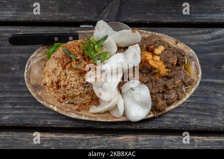 Rending Daging, scharfes indonesisches Eintopf-Rindfleisch und Nasi Goreng, indonesischer oder balinesischer scharfer gebratener Reis auf einem rohen Holztisch. Stockfoto