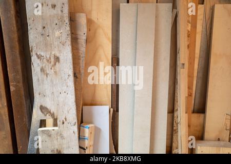 Verschiedene Arten und Seiten von Holzplanken und Holz lehnen sich an der Wand im Werkstattraum an. Stockfoto