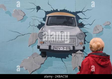 Eine Dame betrachtet ein Wandbild, das der durch die Mauer brechende Trabant, gemalt von Birgits Kinder, einem Teil eines noch stehenden Abschnitts der ehemaligen Berliner Mauer, genannt East Side Gallery, am Vorabend des bevorstehenden 30.. Jahrestages des Mauerfalls. Deutschland feiert diese Woche drei Jahrzehnte seit dem Fall der Berliner Mauer mit den Hauptfeiern in der deutschen Hauptstadt am Samstag, dem 9. November 2019. Am Freitag, den 8. November 2019, in Berlin, Deutschland. (Foto von Artur Widak/NurPhoto) Stockfoto