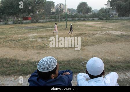 Zwei Jungen beobachten andere Jungen, wie sie am 16. November 2019 in einem lokalen Park in Neu-Delhi, Indien, ein Spiel von „Gilli Danda“ spielen. Es wird mit zwei Stöcken gespielt: Einem großen, einem danda, der verwendet wird, um einen kleineren, den gilli, zu treffen. Es ist ein Sport, der vom indischen Subkontinent stammt und in den ländlichen Gebieten und kleinen Städten in ganz Südasien gespielt wird. (Foto von Mayank Makhija/NurPhoto) Stockfoto