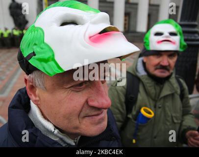 Menschen mit Atemschutzmasken und den Masken von Joker halten die Plakate mit der Aufschrift „Rettet Einzelunternehmer“ auf der Werchowna Rada in Kiew, Ukraine, 3. Dezember 2019. Einige hundert Einzelunternehmer protestieren vor dem ukrainischen Parlament mit der Forderung, das Gesetz abzuschaffen, was nach Ansicht der Demonstranten zur Zerstörung des vereinfachten Systems der Besteuerung, Rechnungslegung und Berichterstattung führen wird. (Foto von Sergii Chartschenko/NurPhoto) Stockfoto