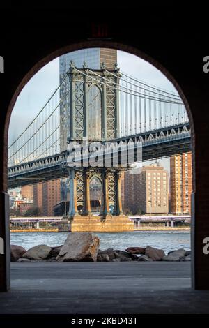 Am frühen Morgen Blick auf die ikonische Manhattan Bridge aus der Sicht des Dumbo Viertels in Brooklyn, NYC, USA am 14. November 2019. Die 448m. Lange Hängebrücke ist ein Wahrzeichen der Stadt New York, eine Touristenattraktion, die den East River überquert und Lower Manhattan mit der Innenstadt von Brooklyn verbindet. Die metallische Eisenbrücke ist aktiv mit Verkehr, 7 Fahrspuren und 4 Bahngleisen für die U-Bahn und Fahrräder. Es wurde 1909 von der Phoenix Bridge Company für den Verkehr geöffnet und von Leon Moisseiff entworfen. (Foto von Nicolas Economou/NurPhoto) Stockfoto