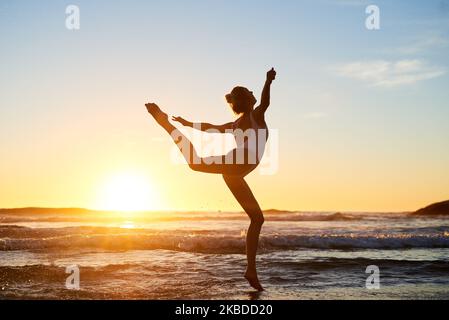 Lebe deine Träume. Silhouette einer jungen Frau gegen einen wunderschönen Sonnenuntergang am Strand. Stockfoto