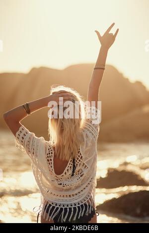 Ich fühle mich am Strand zu Hause. Rückansicht einer jungen Frau am Strand mit der Hand in der Luft. Stockfoto