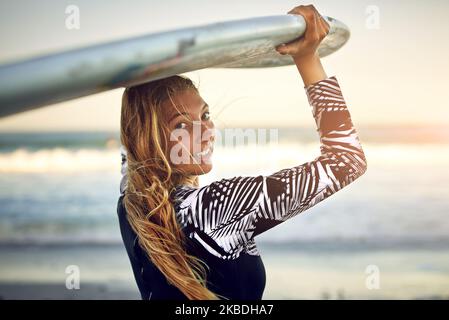 Mach mit. Rückblicksporträt einer attraktiven jungen Surferin, die mit ihrem Surfbrett über den Ozean blickt. Stockfoto