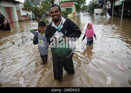 Die Bewohner überqueren die Überschwemmungen, die ihre Siedlungen überfluten, um am 1.. Januar 2020 in das Hochland im Cibitung Regency, West Java, zu fliehen. Der heftige Regen, der seit dem 31. Dezember 2019 mehr als 15 Stunden dauert, verursacht massive Überschwemmungen in der Hauptstadt Jakarta und in einigen Regionen und zwingt Tausende Einwohner zur Flucht. (Foto von Aditya Irawan/NurPhoto) Stockfoto