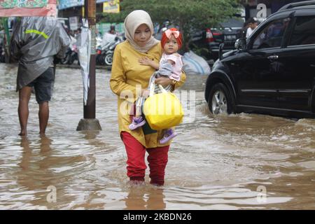 Die Bewohner überqueren die Überschwemmungen, die ihre Siedlungen überfluten, um am 1.. Januar 2020 in das Hochland im Cibitung Regency, West Java, zu fliehen. Der heftige Regen, der seit dem 31. Dezember 2019 mehr als 15 Stunden dauert, verursacht massive Überschwemmungen in der Hauptstadt Jakarta und in einigen Regionen und zwingt Tausende Einwohner zur Flucht. (Foto von Aditya Irawan/NurPhoto) Stockfoto