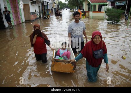Die Bewohner überqueren die Überschwemmungen, die ihre Siedlungen überfluten, um am 1.. Januar 2020 in das Hochland im Cibitung Regency, West Java, zu fliehen. Der heftige Regen, der seit dem 31. Dezember 2019 mehr als 15 Stunden dauert, verursacht massive Überschwemmungen in der Hauptstadt Jakarta und in einigen Regionen und zwingt Tausende Einwohner zur Flucht. (Foto von Aditya Irawan/NurPhoto) Stockfoto