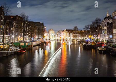 Grachten in Amsterdam wie Amstel mit typischen traditionellen alten niederländischen Architektur Häuser beleuchtet und Hausboote am Abend und Nacht mit schönen Wasserspiegelungen und Stadtlichter, Holland, Niederlande. Amsterdam ist ein Finanzzentrum, aber auch eine der meistbesuchten Städte Europas, die Millionen von Touristen auf der ganzen Welt anzieht, wobei der Tourismus eine wichtige Rolle in der lokalen Wirtschaft spielt, obwohl es Stimmen gegen diese touristische Entwicklung gibt. (Foto von Nicolas Economou/NurPhoto) Stockfoto