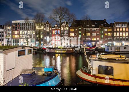 Grachten in Amsterdam wie Amstel mit typischen traditionellen alten niederländischen Architektur Häuser beleuchtet und Hausboote am Abend und Nacht mit schönen Wasserspiegelungen und Stadtlichter, Holland, Niederlande. Amsterdam ist ein Finanzzentrum, aber auch eine der meistbesuchten Städte Europas, die Millionen von Touristen auf der ganzen Welt anzieht, wobei der Tourismus eine wichtige Rolle in der lokalen Wirtschaft spielt, obwohl es Stimmen gegen diese touristische Entwicklung gibt. (Foto von Nicolas Economou/NurPhoto) Stockfoto