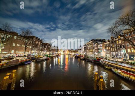 Grachten in Amsterdam wie Amstel mit typischen traditionellen alten niederländischen Architektur Häuser beleuchtet und Hausboote am Abend und Nacht mit schönen Wasserspiegelungen und Stadtlichter, Holland, Niederlande. Amsterdam ist ein Finanzzentrum, aber auch eine der meistbesuchten Städte Europas, die Millionen von Touristen auf der ganzen Welt anzieht, wobei der Tourismus eine wichtige Rolle in der lokalen Wirtschaft spielt, obwohl es Stimmen gegen diese touristische Entwicklung gibt. (Foto von Nicolas Economou/NurPhoto) Stockfoto