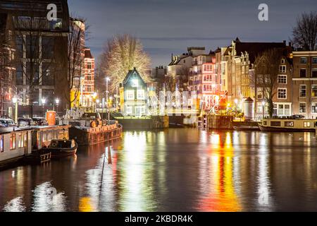 Grachten in Amsterdam wie Amstel mit typischen traditionellen alten niederländischen Architektur Häuser beleuchtet und Hausboote am Abend und Nacht mit schönen Wasserspiegelungen und Stadtlichter, Holland, Niederlande. Amsterdam ist ein Finanzzentrum, aber auch eine der meistbesuchten Städte Europas, die Millionen von Touristen auf der ganzen Welt anzieht, wobei der Tourismus eine wichtige Rolle in der lokalen Wirtschaft spielt, obwohl es Stimmen gegen diese touristische Entwicklung gibt. (Foto von Nicolas Economou/NurPhoto) Stockfoto