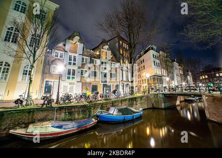 Grachten in Amsterdam wie Amstel mit typischen traditionellen alten niederländischen Architektur Häuser beleuchtet und Hausboote am Abend und Nacht mit schönen Wasserspiegelungen und Stadtlichter, Holland, Niederlande. Amsterdam ist ein Finanzzentrum, aber auch eine der meistbesuchten Städte Europas, die Millionen von Touristen auf der ganzen Welt anzieht, wobei der Tourismus eine wichtige Rolle in der lokalen Wirtschaft spielt, obwohl es Stimmen gegen diese touristische Entwicklung gibt. (Foto von Nicolas Economou/NurPhoto) Stockfoto