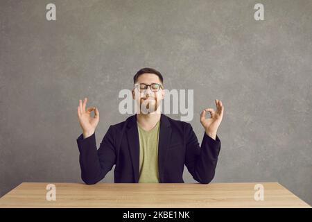 Ruhiger Mann, der am Schreibtisch sitzt, meditiert, Yoga macht und Stress lindert Stockfoto