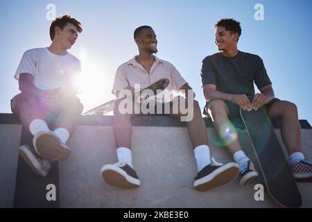 Vielfalt, Freunde und Männer mit Skateboard reden gemeinsam an der Wand in der Stadt. Fröhliches Gespräch, Lachen und eine Freundschaftsgruppe mit dem Gen z Skater Stockfoto
