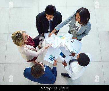 Weitergabe einiger wichtiger Unterlagen. Eine Aufnahme aus dem Blickwinkel einer Gruppe von Geschäftsleuten, die in einem Büro Papierkram durchmachen. Stockfoto