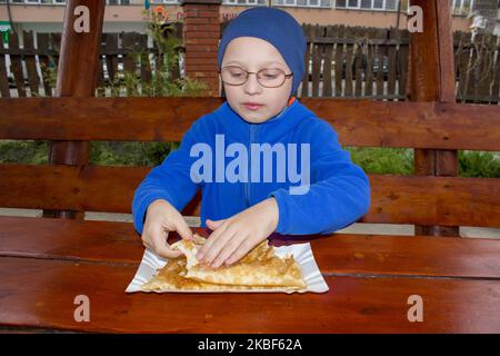 Baby im Herbst isst eine Mahlzeit am Tisch Kuchen mit Fleisch Stockfoto