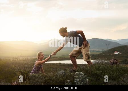 Die Natur bringt das Beste in allen hervor. Ein freundlicher junger Wanderer hilft seinem Freund, auf einem Bergpfad auf einen Felsen zu klettern. Stockfoto