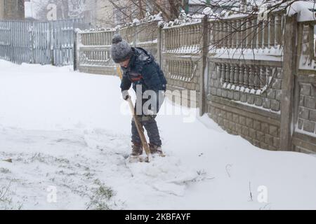 Der Junge im Schneesturm im Winter reinigt den Schnee mit einer Schaufel Stockfoto