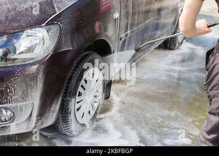 Mann, Waschen seines Autos Räder einer Autowäsche, mit einem Hochdruckwasserstrahl Stockfoto